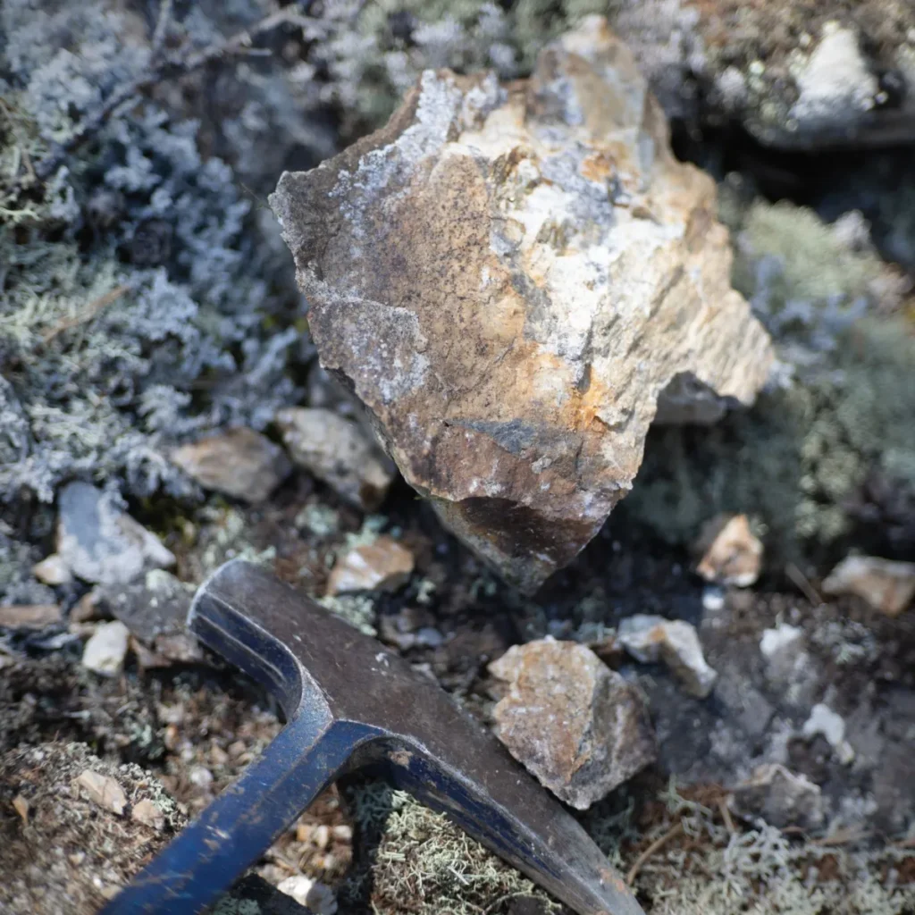 Rock hammer beside a mineral specimen on rocky ground while rockhounding
