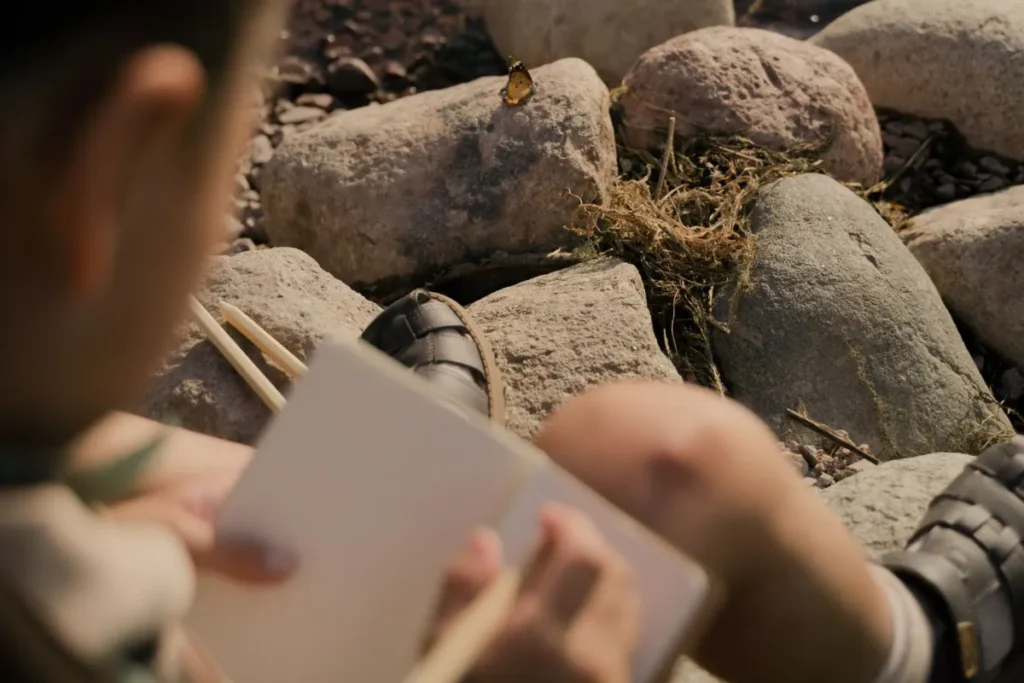Person writing notes in a notebook beside a pile of smooth rocks
