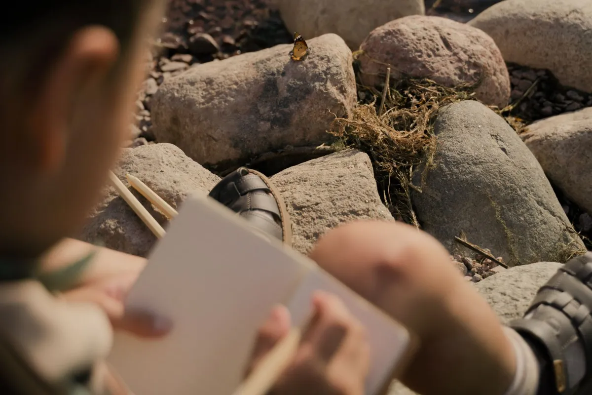 Person writing notes in a notebook beside a pile of smooth rocks