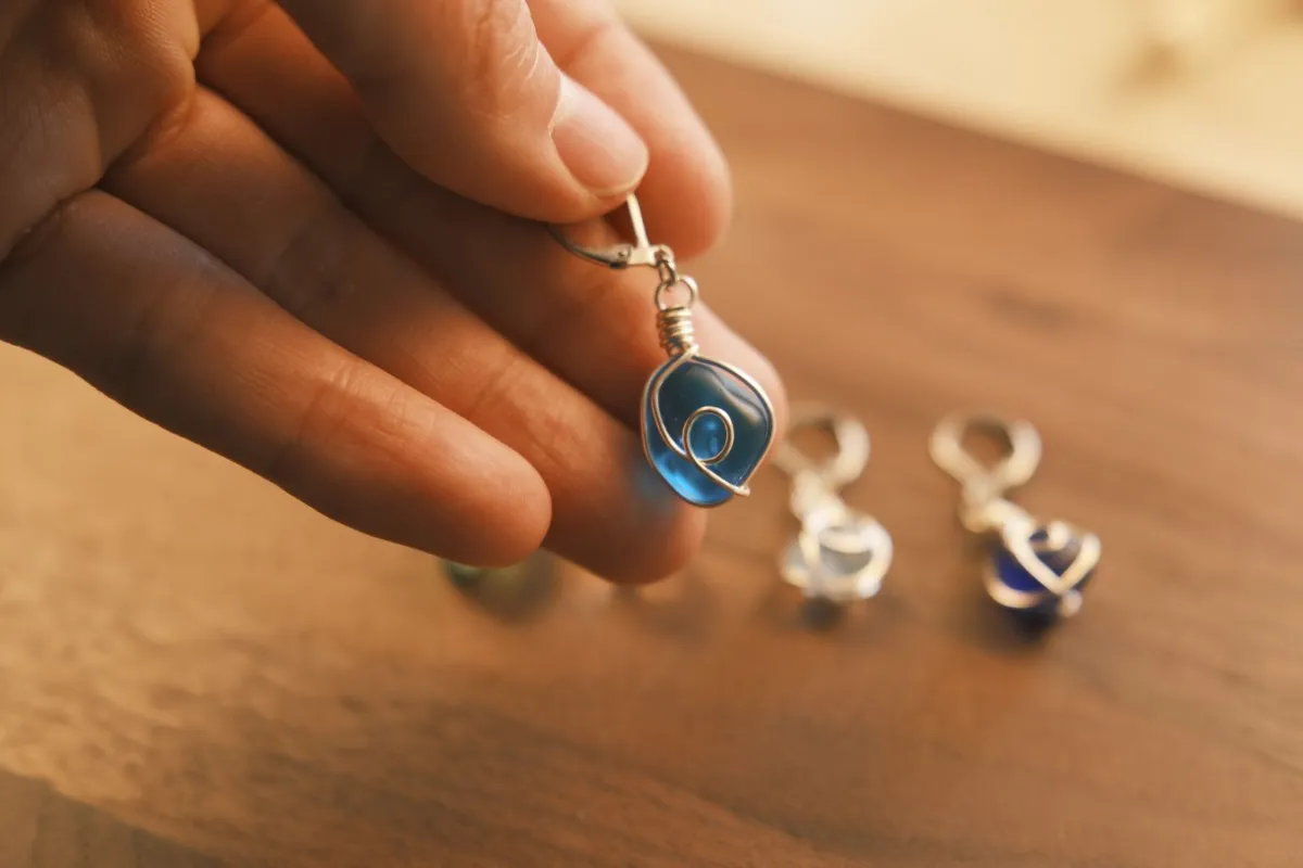 Wire-wrapped blue sea glass earrings held in a hand